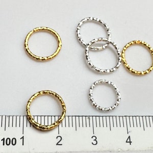 May include: Five jump rings, two gold and three silver, with a textured finish. The rings are approximately 1 inch in diameter and are shown next to a ruler.