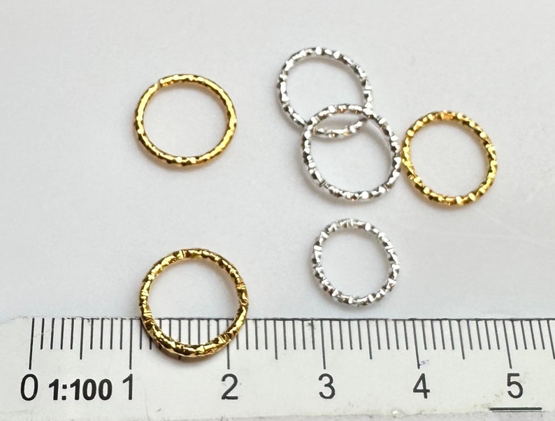 May include: Five jump rings, two gold and three silver, with a textured finish. The rings are approximately 1 inch in diameter and are shown next to a ruler.
