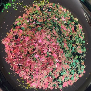 May include: Close-up of a black bowl filled with a mix of glitter. The glitter is a mix of pink, green, and iridescent colors. The glitter is in various shapes and sizes, reflecting light.