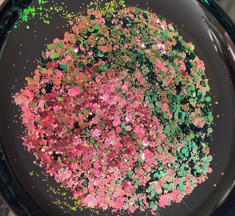 May include: Close-up of a black bowl filled with a mix of glitter. The glitter is a mix of pink, green, and iridescent colors. The glitter is in various shapes and sizes, reflecting light.