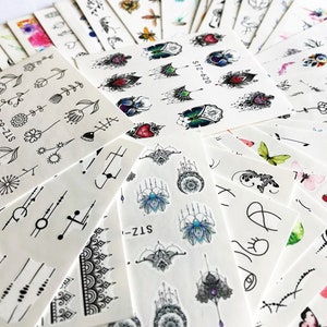 Könnte beinhalten: Sortiment an temporären Tattoo-Blättern mit verschiedenen Designs, darunter Blumen, Schmetterlinge, geometrische Formen und Mandalas. Die Blätter sind weiß mit schwarzer Tinte und einige haben farbige Akzente.
