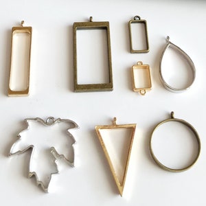 Op de afbeelding: Assortiment van acht verschillende metalen hangerframes voor het maken van harssieraden. De frames zijn in verschillende vormen, waaronder een rechthoek, een cirkel, een traan, een driehoek en een blad. De frames zijn gemaakt van goud en zilver metaal.