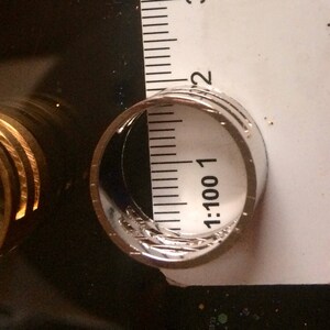 May include: Close-up of a silver ring with a textured design, next to a ruler. The ring appears to be approximately 0.75 inches in diameter. The ring is on a dark surface.