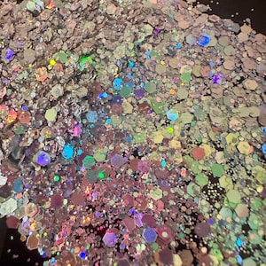 May include: A pile of iridescent glitter with a mix of hexagonal and irregular shapes. The glitter reflects a rainbow of colors, including pink, green, blue, and purple, creating a shimmering effect. Ideal for crafts and decorations.