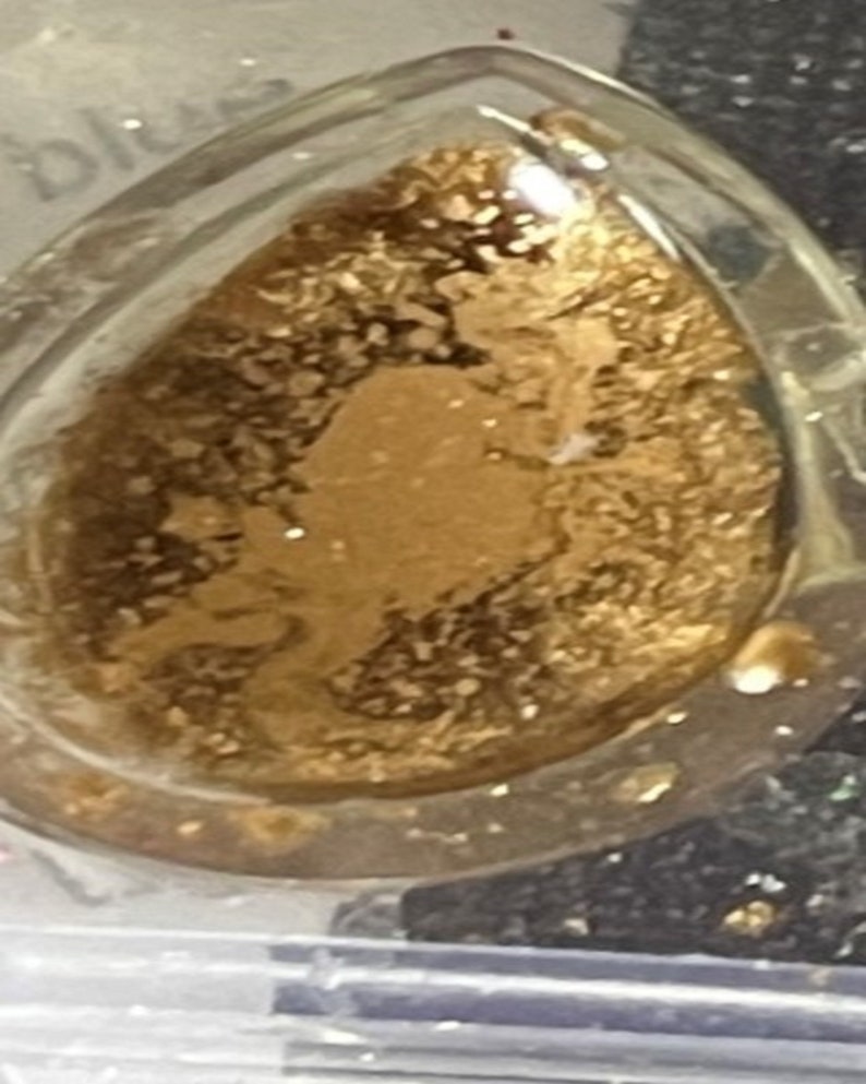 K&ouml;nnte beinhalten: Ein klarer, tropfenf&ouml;rmiger Anh&auml;nger gef&uuml;llt mit Goldflocken. Der Anh&auml;nger hat einen transparenten Rand und ein goldenes Inneres, wodurch ein schimmernder Effekt entsteht. Das Design ist schlicht und elegant, geeignet f&uuml;r Schmuck.