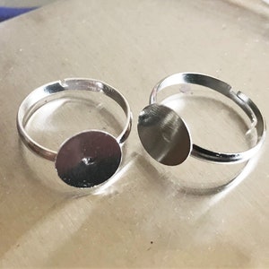 Op de afbeelding: Twee verstelbare zilveren ringen met ronde, platte, zilverkleurige metalen bases. De bases zijn ontworpen om een cabochon of andere versiering te houden.