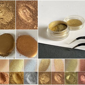 K&ouml;nnte beinhalten: Nahaufnahmen verschiedener gold- und bronzefarbener Lidschattenpigmente. Das Bild zeigt ein kleines Glas mit goldenem Lidschatten, Farbmuster und Nahaufnahmen der Texturen. Die Farben reichen von hellgold bis tiefbronze, mit unterschiedlichen Texturen und Finishes. Auch eine Pinzette ist zu sehen.