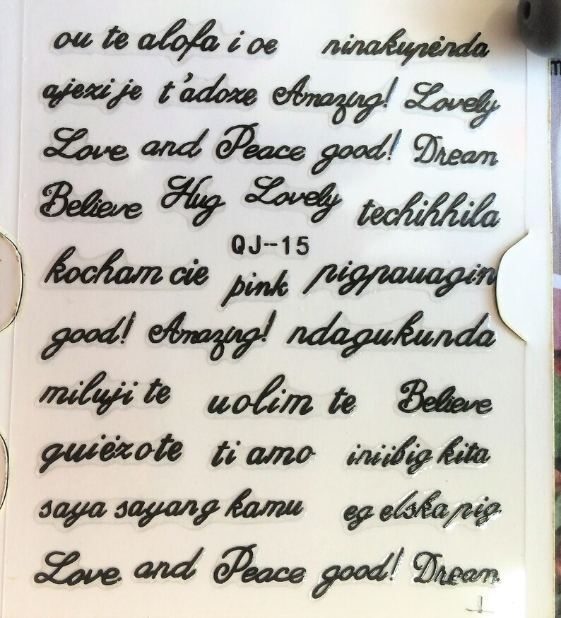 May include: A sheet of clear stickers with black lettering. The stickers feature phrases in different languages, including "Love and Peace", "Amazing!" and "Believe".