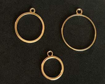 May include: Three gold-colored metal circles with a loop at the top. The circles are different sizes and are arranged in a row on a black surface.