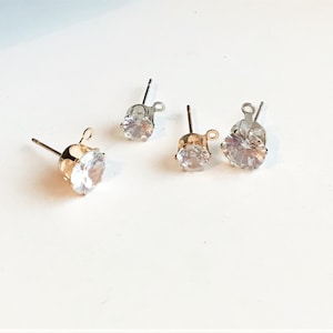Op de afbeelding: Drie paar oorbelsluitingen met heldere ronde strass steentjes. De sluitingen zijn gemaakt van goud en zilverkleurig metaal.