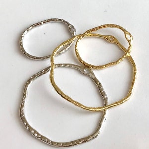 May include: Four metal rings, two gold and two silver, with textured surfaces. The rings are oval shaped and have a small hole at the top.
