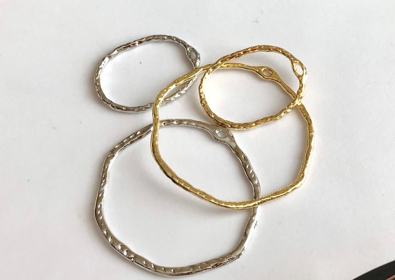 May include: Four metal rings, two gold and two silver, with textured surfaces. The rings are oval shaped and have a small hole at the top.
