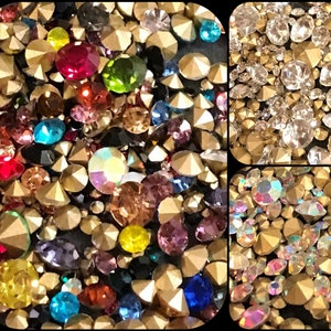 May include: Assortment of colorful and clear rhinestones with gold settings. The rhinestones are in various shapes and sizes.