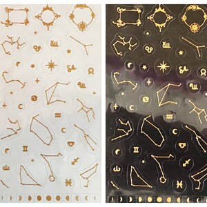 May include: Two sheets of gold constellation stickers, one on a white background and one on a black background. The stickers feature various constellations, stars, and celestial symbols.