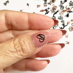 May include: A close-up of a finger with a black heart-shaped nail sticker that says "Love" on it. The sticker is on a nude-colored nail.