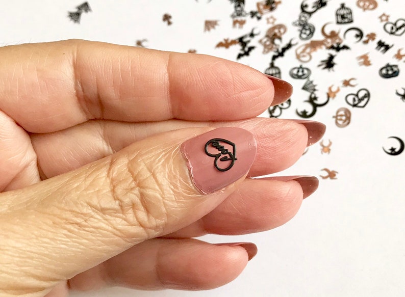 May include: A close-up of a finger with a black heart-shaped nail sticker that says "Love" on it. The sticker is on a nude-colored nail.