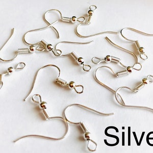 May include: Silver earring hooks with a spring clasp and a small ball at the end. The hooks are scattered on a white surface.