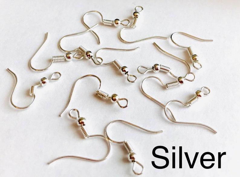 May include: Silver earring hooks with a spring clasp and a small ball at the end. The hooks are scattered on a white surface.