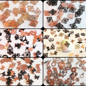 May include: Assortment of small metal charms in various shapes and designs, including butterflies, cages, gears, and gothic-inspired patterns. The charms are in gold, black, and copper tones.