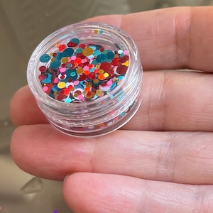 Pu&ograve; includere: Un piccolo barattolo trasparente pieno di glitter rotondi colorati. Il glitter &egrave; un mix di rosso, verde, oro e bianco.