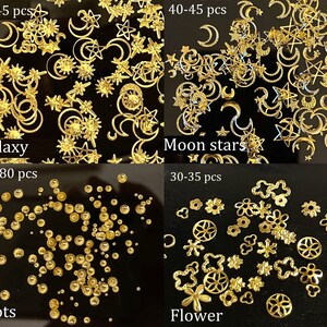 Op de afbeelding: Vier sets gouden nagelcharms op een zwarte achtergrond. De eerste set is gelabeld "Galaxy" en bevat 70-80 stuks sterren, manen en zonnen. De tweede set is gelabeld "Moon stars" en bevat 40-45 stuks manen en sterren. De derde set is gelabeld "Dots" en bevat 70-80 stuks kleine gouden stippen. De vierde set is gelabeld "Flower" en bevat 30-35 stuks gouden bloemvormen.