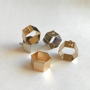 May include: Four hexagonal metal pendant charms, two gold and two silver, with a loop at the top for attaching to jewelry or other crafts.