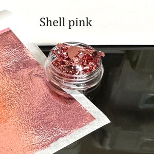 May include: A small clear jar filled with loose, thin, metallic flakes in a shell pink color. The text "Shell pink" is written above the jar.