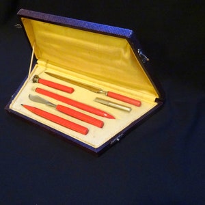 May include: A set of six red handled tools in a brown leather case. The tools include a letter opener, a small knife, a pencil, a small brush, and two small tools with red handles.