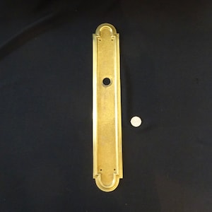 May include: A gold-toned door plate with a decorative design and a keyhole. The plate is about 10 inches tall and 2 inches wide.