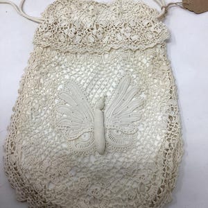 May include: A white crocheted drawstring bag with a butterfly design. The bag has a delicate lace pattern and a long white cord.