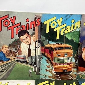 May include: A collection of vintage Toy Trains magazines featuring colorful covers with illustrations of trains and children. The covers feature the text "Toy Trains" and "The Milwaukee Road".