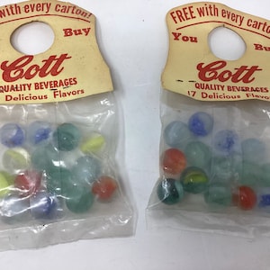 May include: Two clear plastic bags with red and white hang tags that say "FREE with every carton! You Buy Cott QUALITY BEVERAGES 17 Delicious Flavors". Each bag contains a variety of colorful marbles.