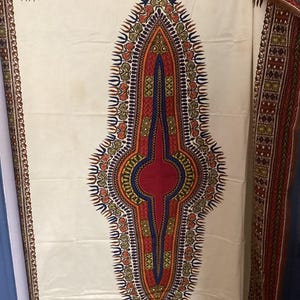 May include: White fabric with a red, blue, and gold geometric pattern. The pattern is a large, teardrop-shaped design with a smaller circle in the center.