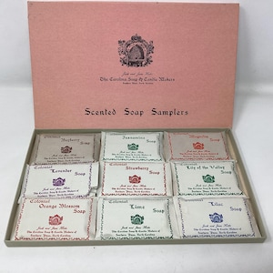 May include: A pink box with a lid, containing a selection of scented soap samplers. The box is labeled "Scented Soap Samplers" and features various soap scents like "Bayberry", "Lavender", and "Orange Blossom".