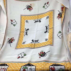 May include: White tablecloth with a yellow brick pattern border. The center features a repeating pattern of black silhouettes of horse-drawn carriages. The border also features images of a rooster, a scale, and a cart with flowers.