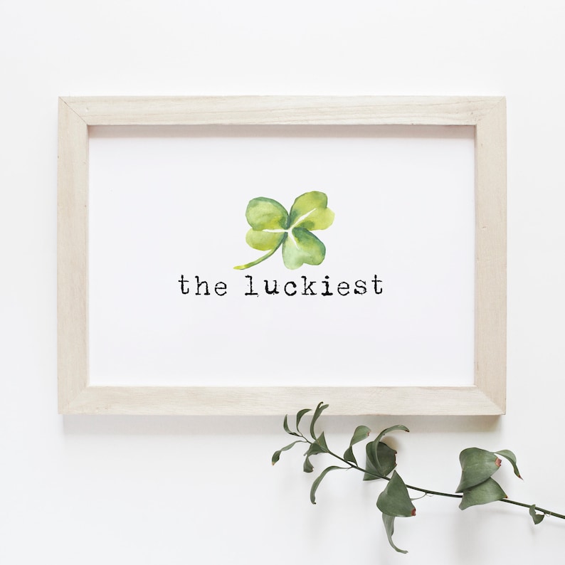 May include: A white framed print with a watercolor painting of a four-leaf clover and the text "the luckiest".