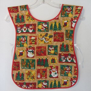 Puede incluir: Un delantal de Navidad rojo y blanco con fondo marr&oacute;n. El delantal presenta una variedad de dise&ntilde;os festivos, incluyendo mu&ntilde;ecos de nieve, renos y &aacute;rboles de Navidad.