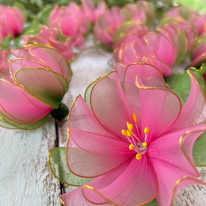 May include: A cluster of pink and green fabric flowers with gold trim. The flowers are made of sheer fabric and have a delicate, layered appearance.