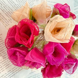 May include: A bouquet of delicate paper flowers in shades of pink and cream. The flowers are made from thin, translucent material and have a delicate, romantic look.