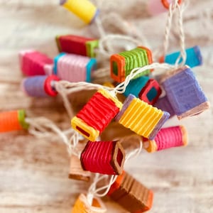 K&ouml;nnte beinhalten: Eine Lichterkette mit bunten Papierlaternen und einem wei&szlig;en Kabel. Die Laternen haben verschiedene Formen und Gr&ouml;&szlig;en, einige haben ein gefaltetes Design.