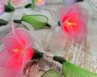 May include: String of fairy lights with pink and green flower-shaped fabric covers. The lights are lit and glowing.