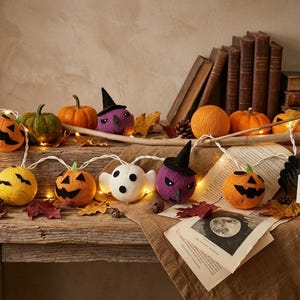 Puede incluir: Una guirnalda de luces de Halloween con adornos de fieltro hechos a mano, incluyendo calabazas naranjas, un fantasma blanco, una bruja morada y una araña negra. Un letrero dice Handcrafted Felt Halloween Lights - Artisan Collection.