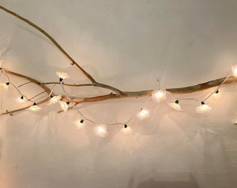 May include: White string lights with flower-shaped bulbs are strung along a branch, creating a whimsical and decorative display.