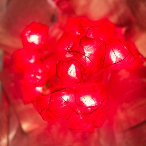 Puede incluir: Un grupo de objetos brillantes de color rojo, de forma geométrica, posiblemente luces o adornos decorativos. Los objetos tienen una apariencia facetada y están iluminados, creando un efecto brillante. El fondo es un rojo suave y borroso.