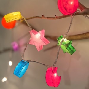 May include: String of lights with paper lanterns shaped like stars, moons, and circles in various colors, including pink, blue, yellow, and green.