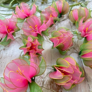 May include: Pink and green flower shaped string lights. The lights are made of fabric and have a gold wire running through them.