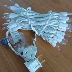May include: A bundle of white Christmas lights with clear bulbs and a white cord. The electrical plug and fuse are also white. The text on the plug reads "125V FUSE" and "USE ONLY".