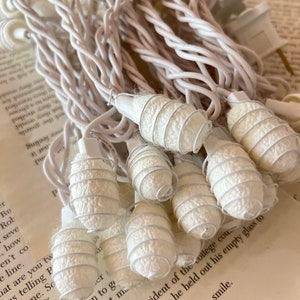 May include: White string lights with white fabric covered bulbs. The bulbs are shaped like a spiral. The lights are coiled up on a table.