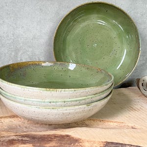 May include: A set of four green and white speckled ceramic bowls. The bowls are stacked on top of each other, with the largest bowl at the bottom and the smallest bowl at the top. The bowls are sitting on a wooden surface.