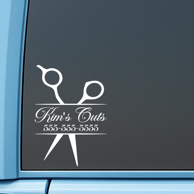 May include: A white vinyl decal applied to a dark window, featuring a graphic of a pair of scissors. The text Kim's Cuts is written in a cursive script, followed by the phone number 555-555-5555, all centered within the scissor design.
